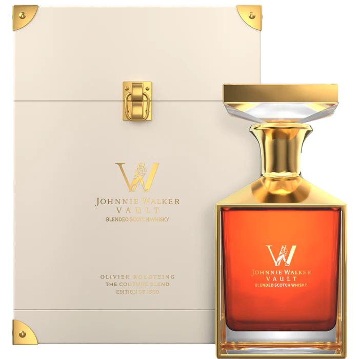 A luxurious Johnnie Walker Vault: The Couture Blend Olivier Rousteing 700ml decanter with a gold-accented stopper sits before an elegant cream and gold display case featuring gold lettering and trim.