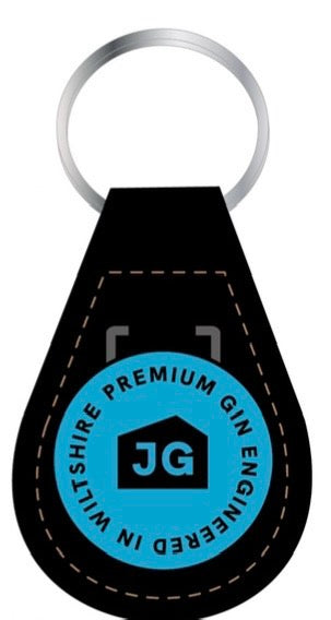 The James Gin The Tupac 2 Bottle Set W/ Souvenir Gift Key Chain by James Gin US includes a black leather keychain with brown stitching and a blue emblem reading 'PREMIUM JAMES GIN ENGINEERED IN WILTSHIRE' with 'JG' in a house icon, reflecting British craft gin quality.