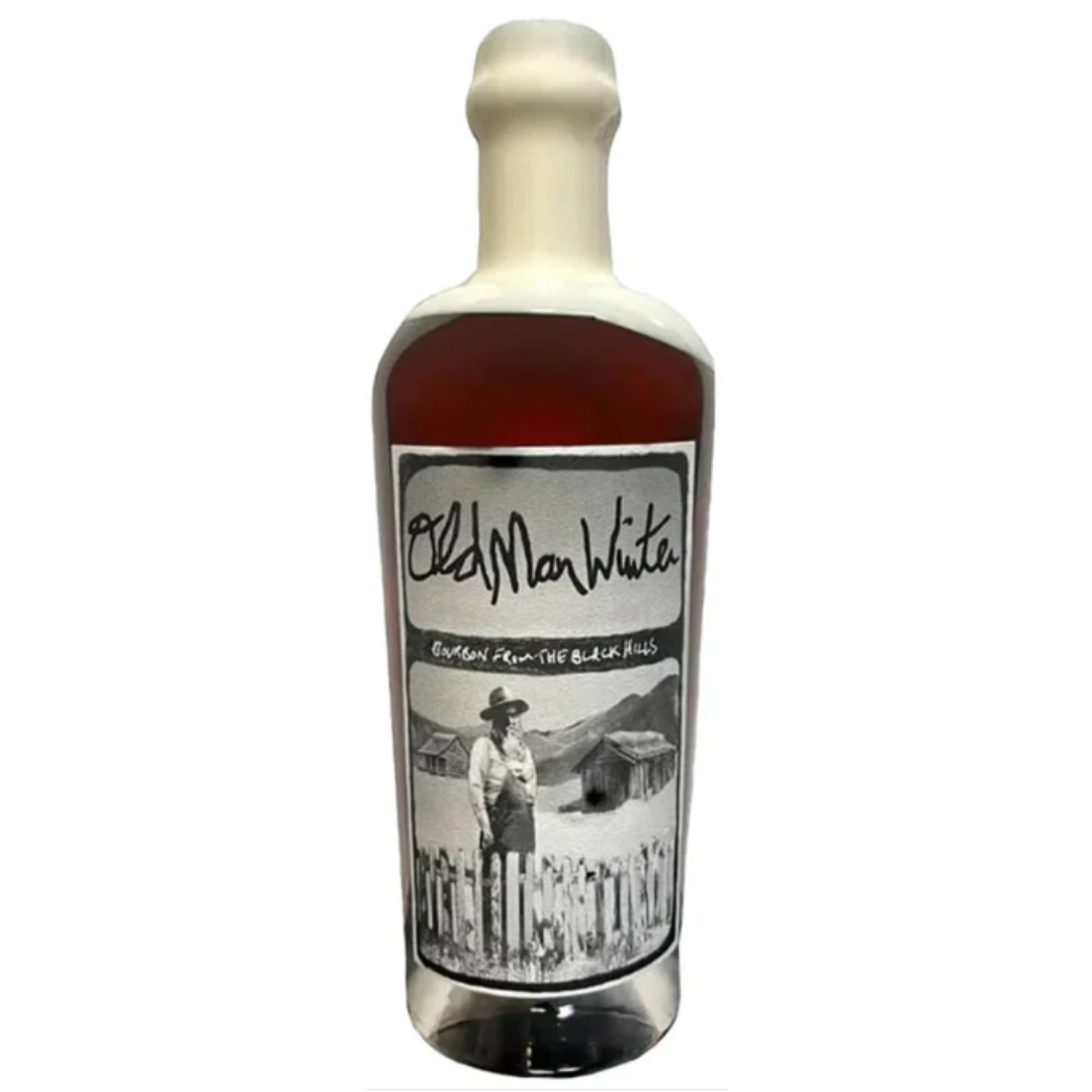 A bottle of Old Man Winter Four Grain Small Batch Bourbon by Olde St. Nick, sealed in white wax with a label featuring a black-and-white photo of a man by a fence, cabins, and mountains—a tribute to true American craft distilling.